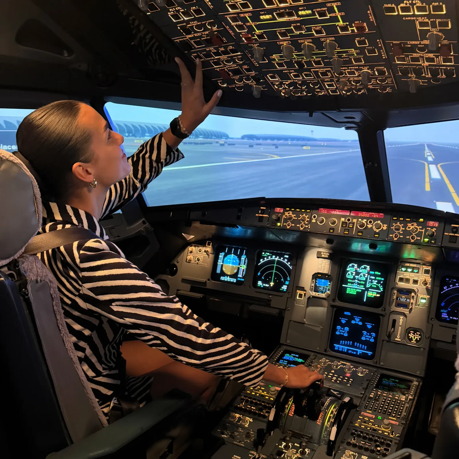 Emilia reaching for the overhead panel in the A320 cockpit